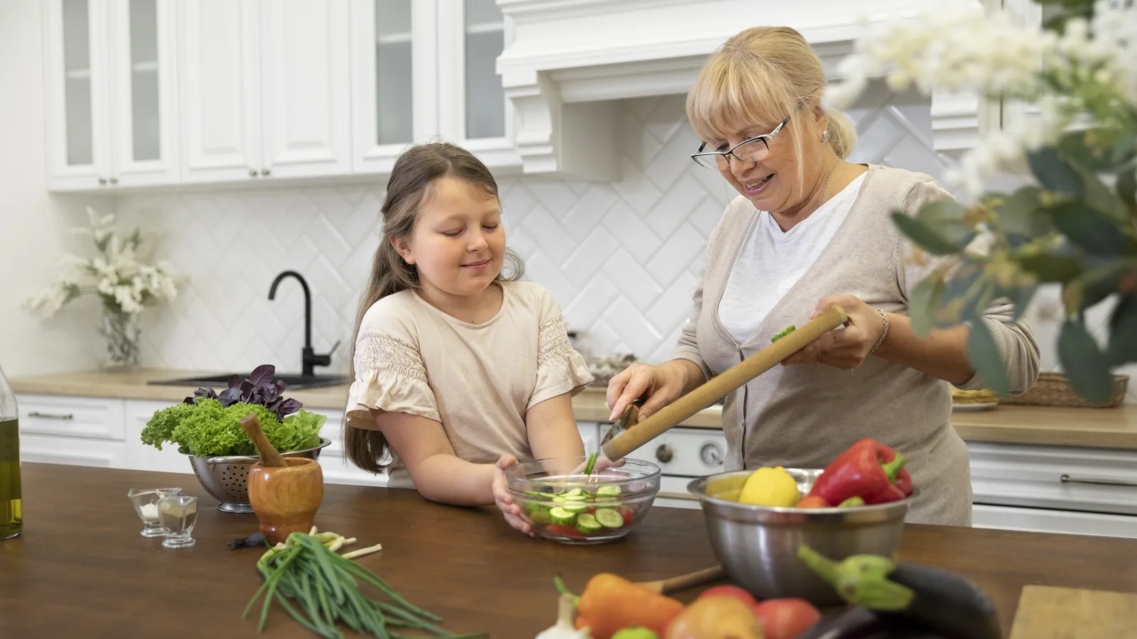 An older woman and a girl arranging a salad bowl together at a kitchen counter