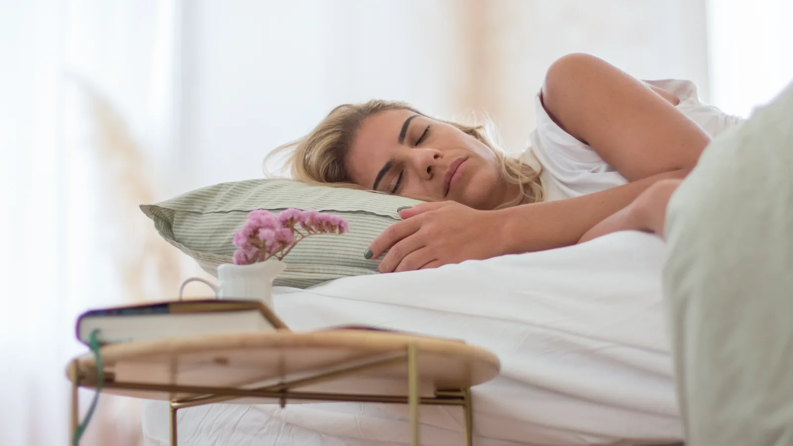 Woman asleep in white bed linen in soft morning light